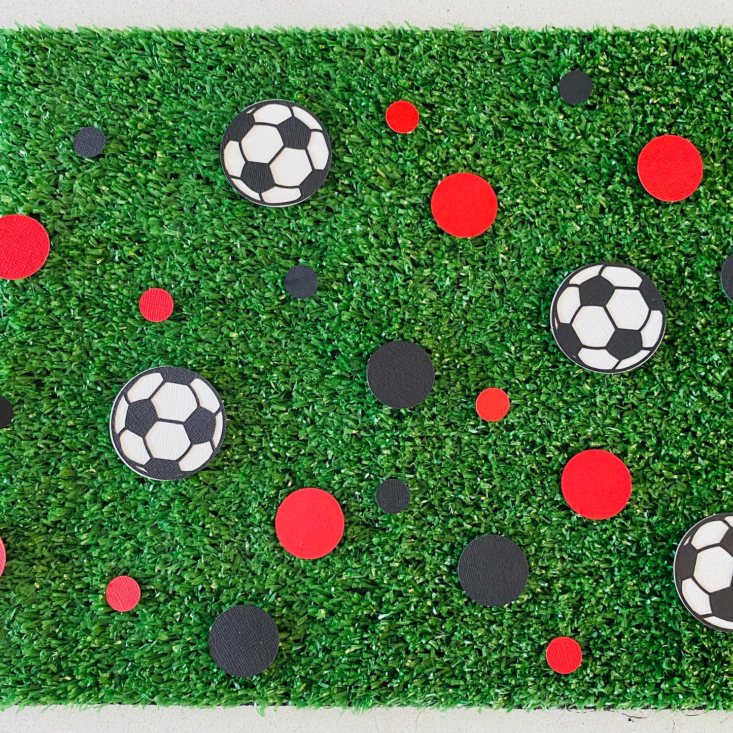 Red and black paper round discs with soccer ball paper discs  scattered across green grass.