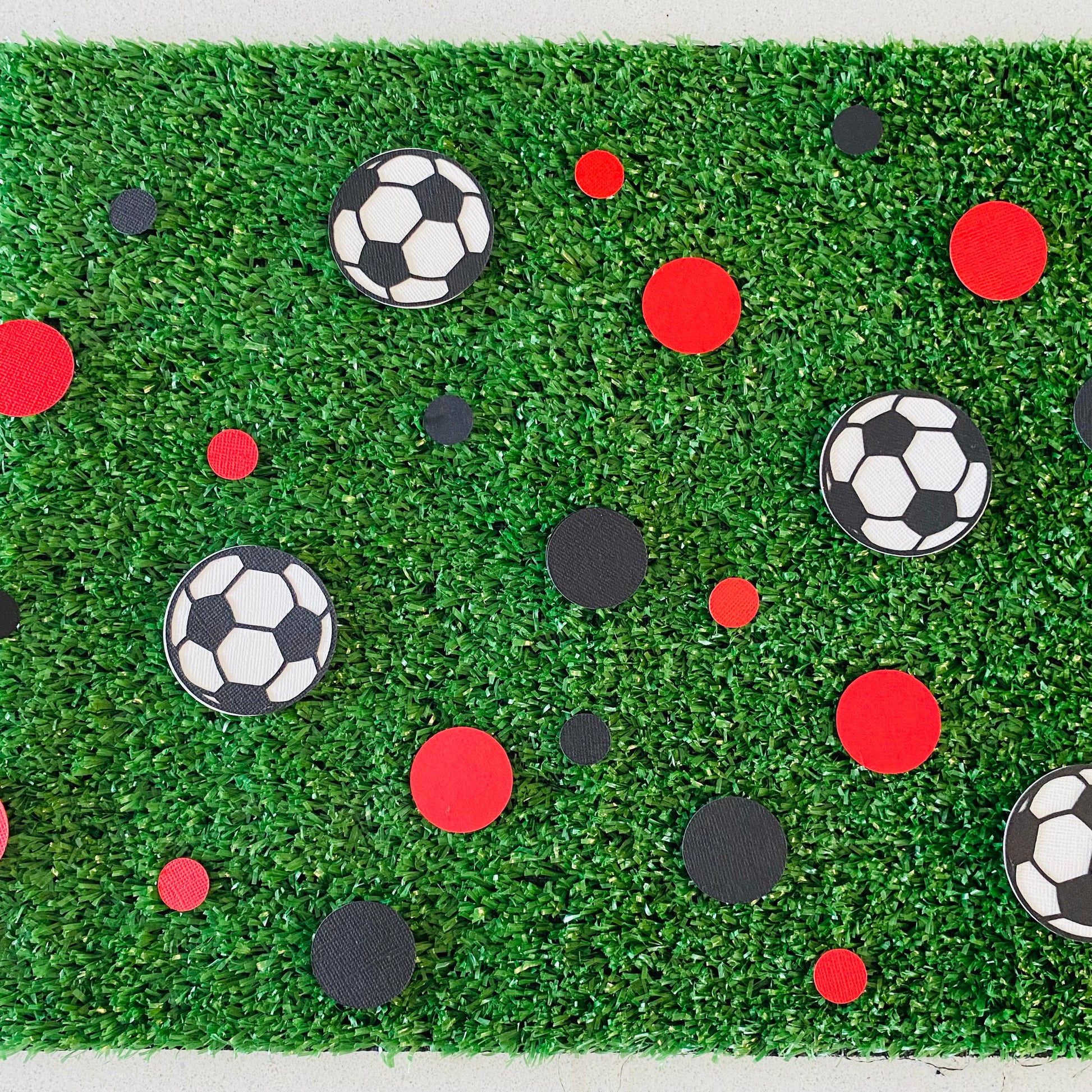Red and black paper round discs with soccer ball paper discs  scattered across green grass.