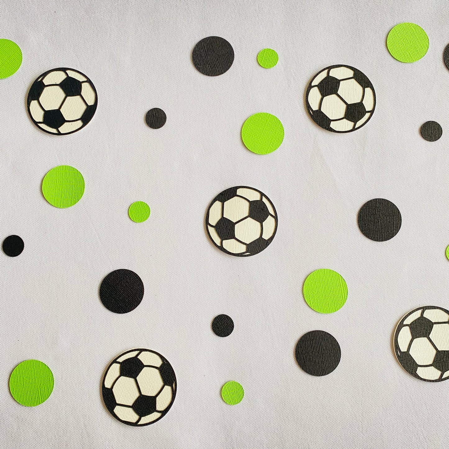 Green and black round paper cutouts with soccer ball cutouts spread on a white table