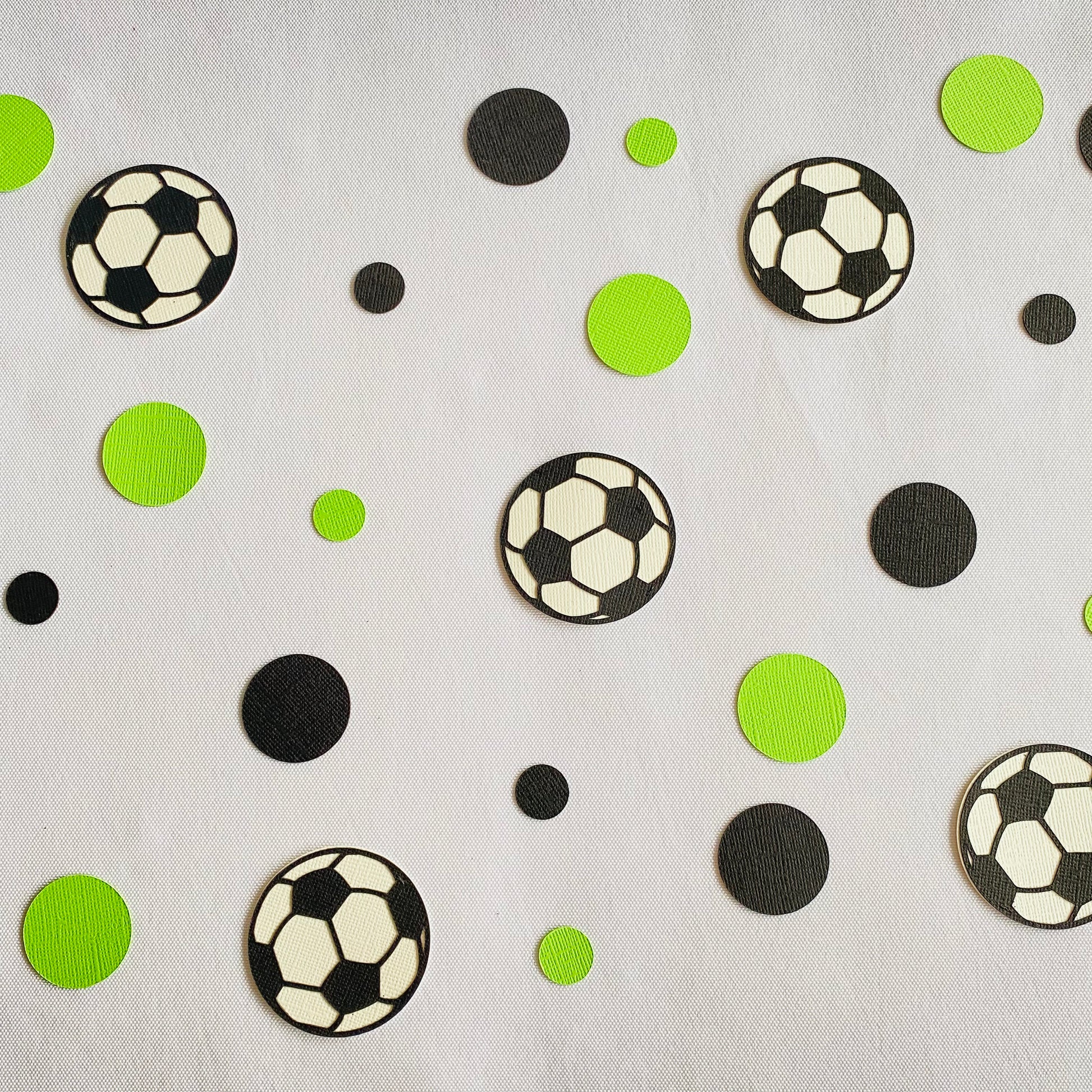 Green and black round paper cutouts with soccer ball cutouts spread on a white table