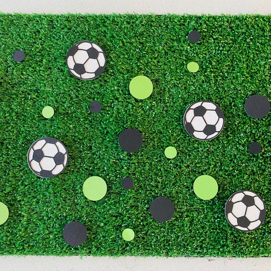 Green and Black round paper cutouts with soccer ball cutouts spread on synthetic grass